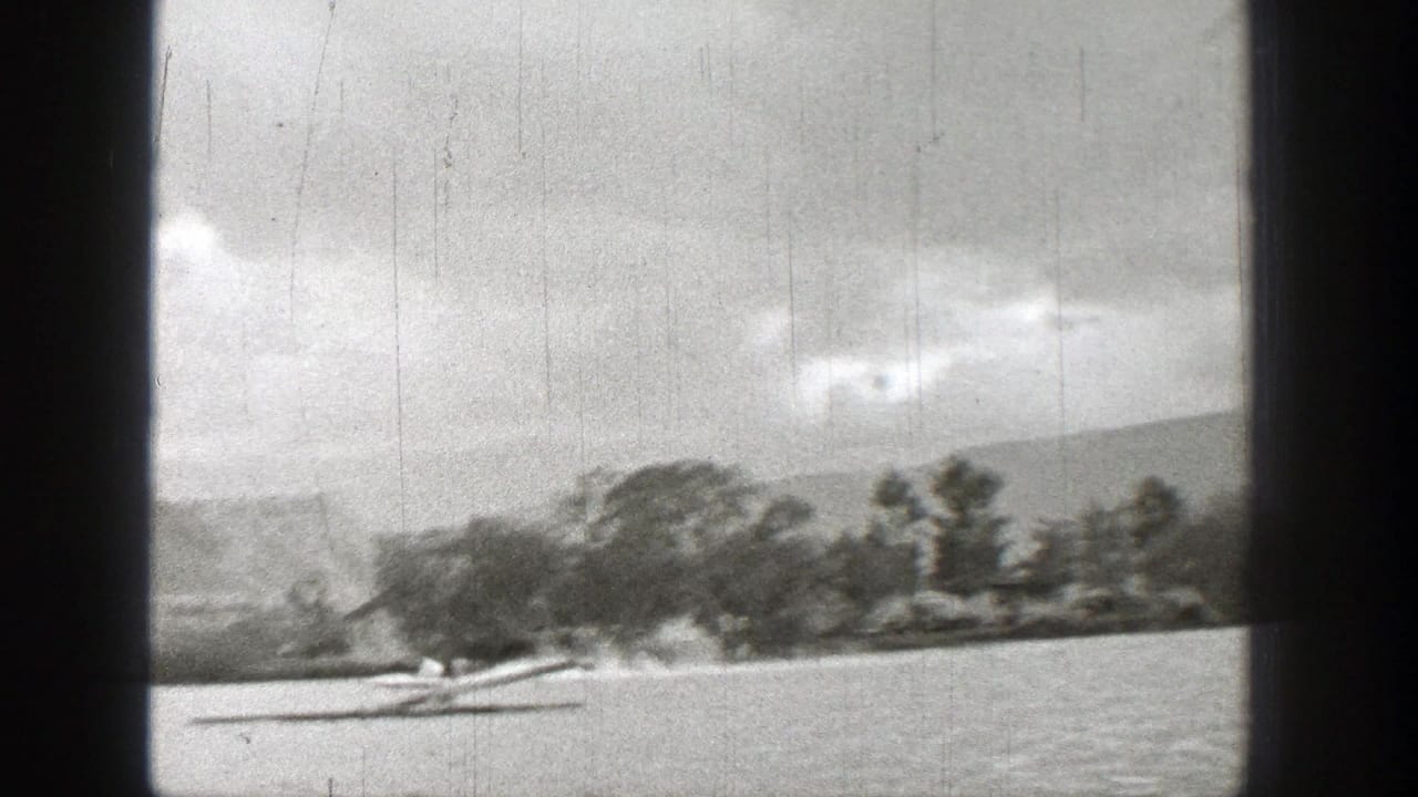 Speeding boat on a lake leaving spray and wake beside a wooded shoreline.