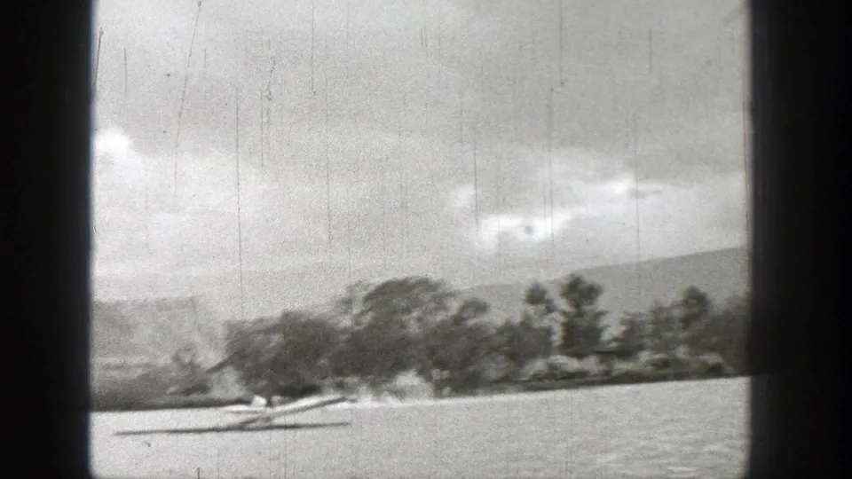 1938 Washington home-movie frame of a motorized watercraft throwing wake on a lake near trees and low mountains.