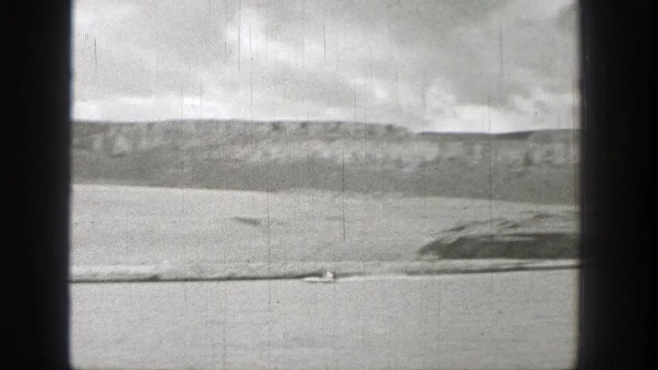 Final 1938 Washington 8mm frame showing a small watercraft crossing a lake beneath low hills and cloudy sky.