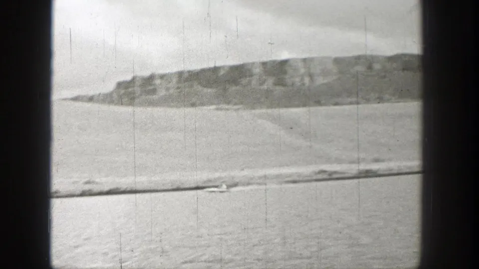 Black-and-white 8mm view of a small boat on a Washington river with rocky hills beyond.