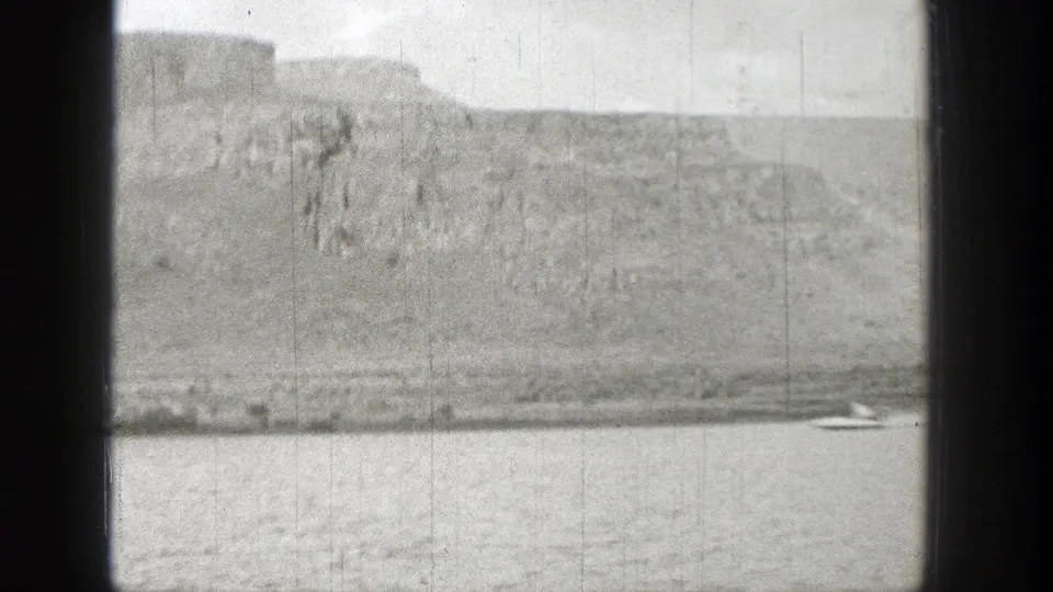 1938 home-movie frame of a boat near the riverbank below steep Washington cliffs.