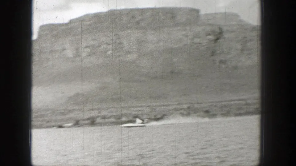 Black-and-white Washington river view with a small boat leaving a wake below a rocky hillside.