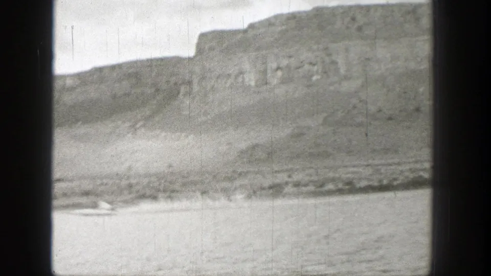 1938 Washington home-movie frame showing a lake below rocky mountain cliffs, with dark gate edges and no discernible people.