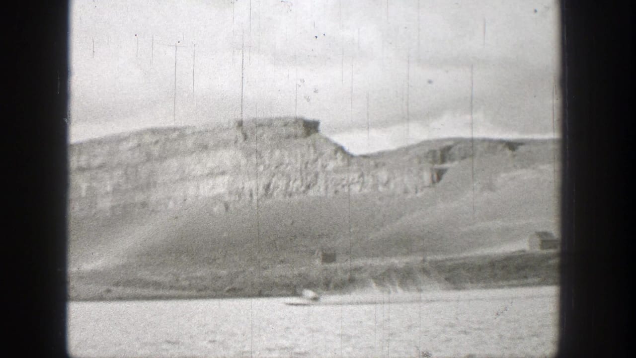 Small motorboat on a lake beneath rocky hills and cliffs.