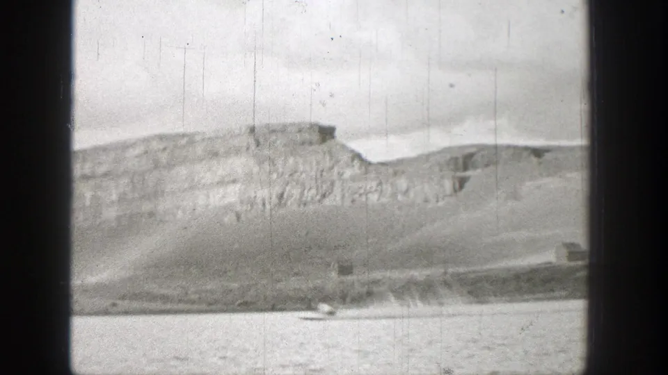 A distant small motorboat crosses a Washington mountain lake in 1938 home-movie footage, with rocky slopes behind it.