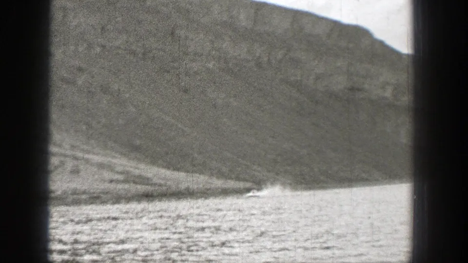A small motorboat leaves a bright wake on a lake below a rugged Washington mountainside in the 1938 home-movie clip.