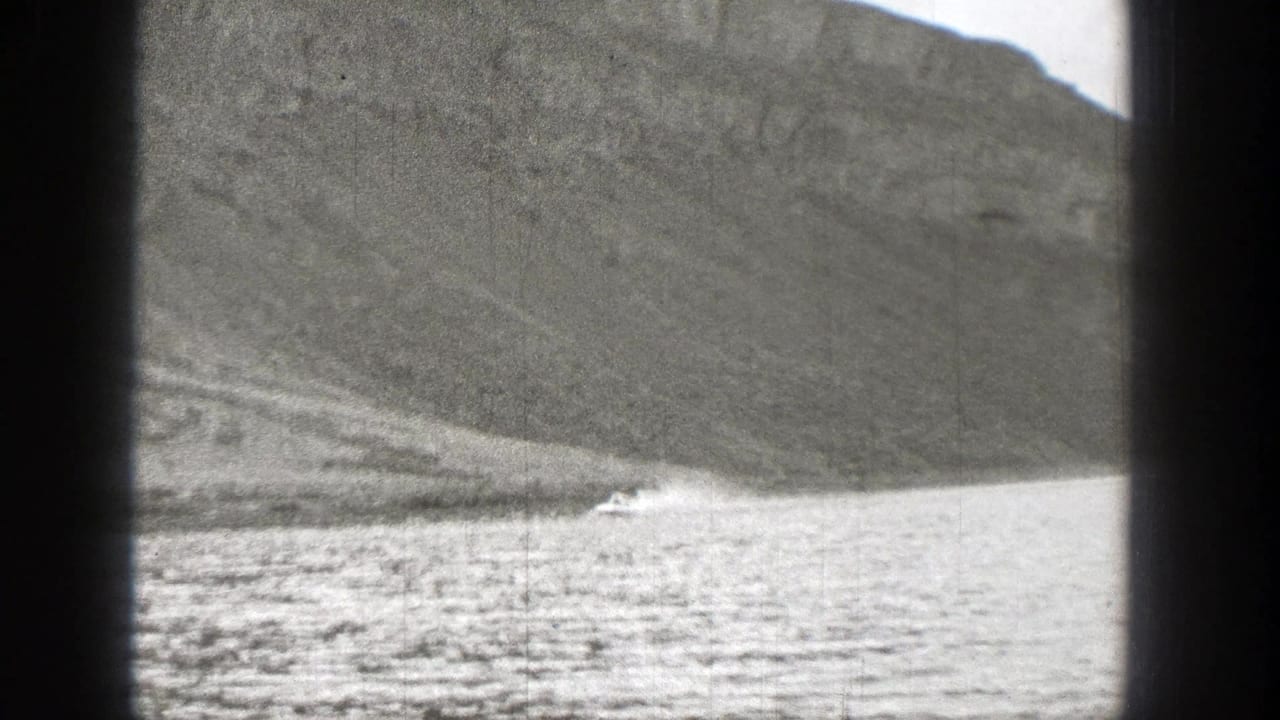 Motorboat crossing a lake below a steep mountain slope.