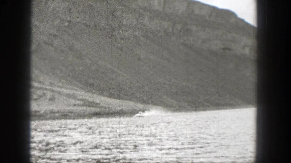 1938 Washington home-movie frame showing a small motorboat on a lake with a rugged mountain rising behind it.