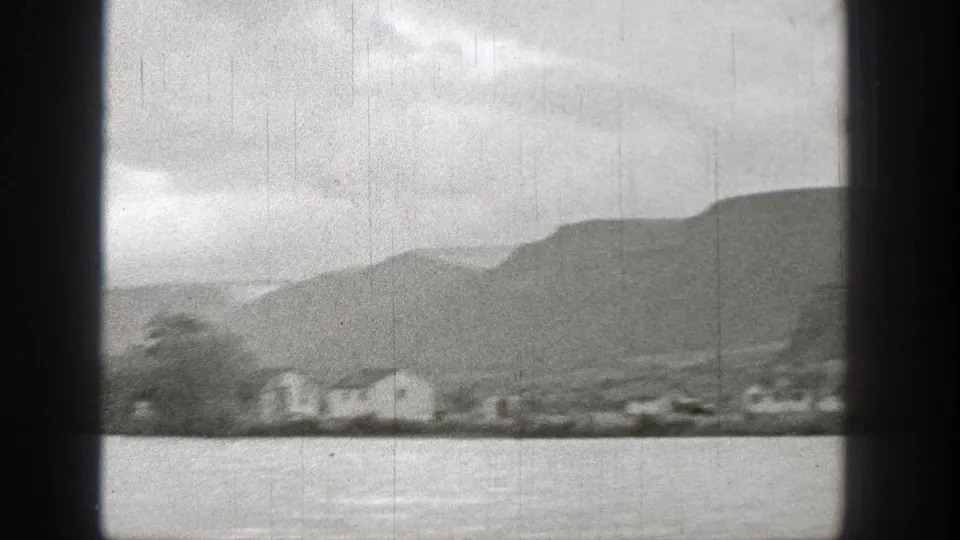 Washington lake view with small shoreline houses, trees, low mountains, and cloudy sky in a 1938 home-movie frame.