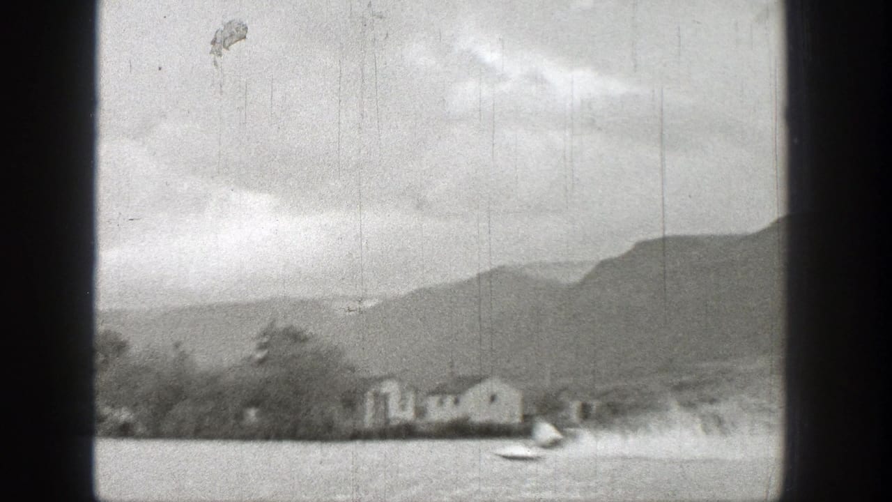 1938 Washington 8mm frame showing a fast motorboat crossing a lake near distant houses, trees, and hills.