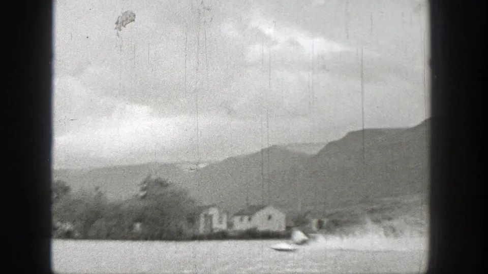 1938 Washington 8mm frame showing a fast motorboat crossing a lake near distant houses, trees, and hills.