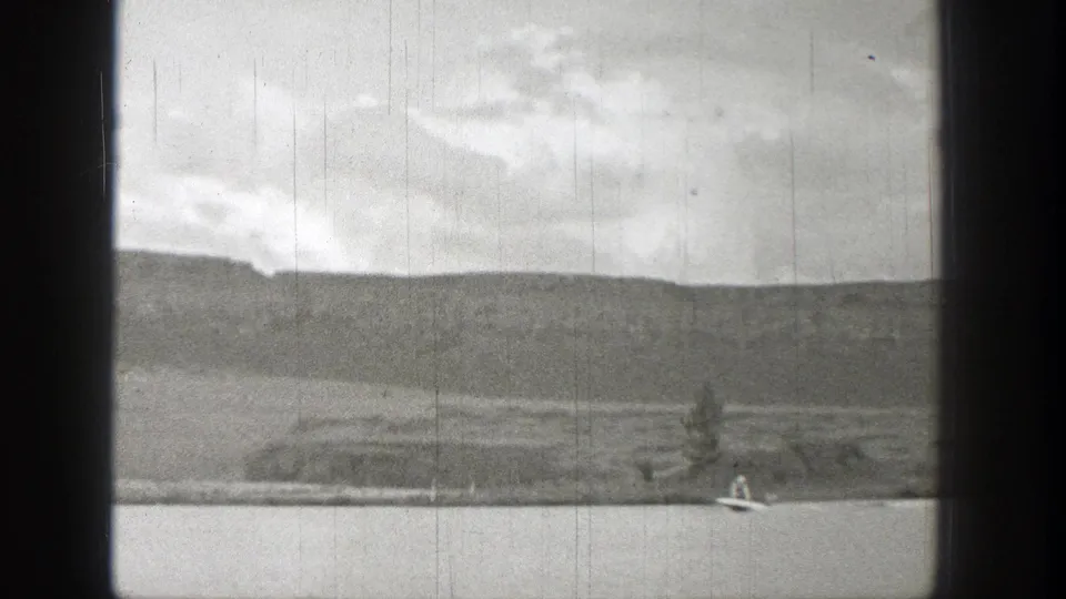 1938 Washington home-movie frame with a motorboat low in the shot, open lake water, shoreline, hills, and clouds.
