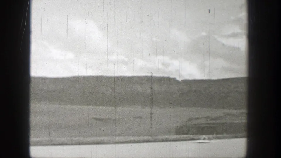 1938 Washington 8mm frame showing a distant small watercraft moving along a calm river below a low hillside.