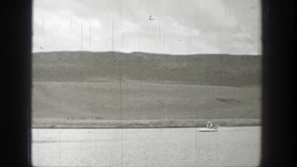 A distant rider on a small watercraft passes along the Washington riverbank in this 1938 home-movie frame.