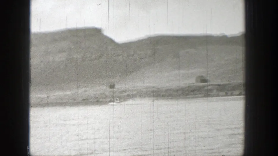 Final 1938 Washington frame with a small dark waterborne object near shore, backed by layered hills and visible film wear.