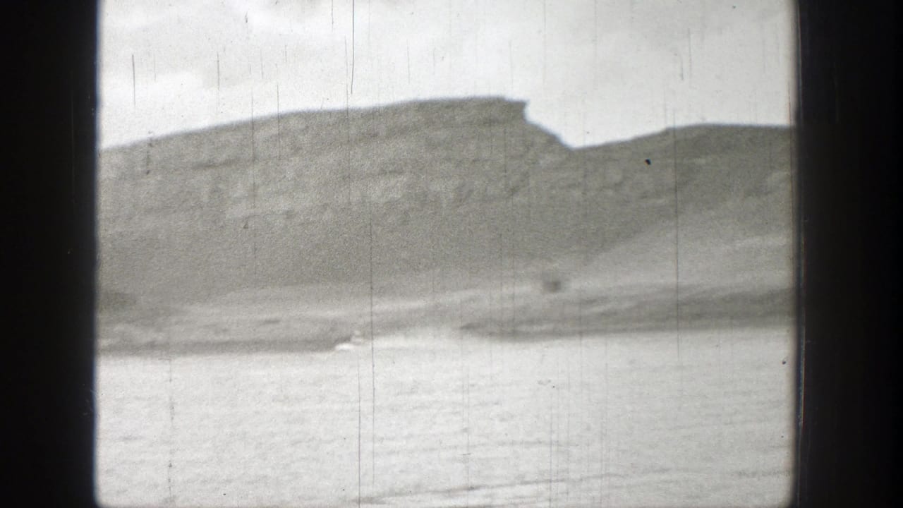 1938 Washington 8mm frame showing a broad lake surface below a soft, rocky mountain ridge under cloudy sky.