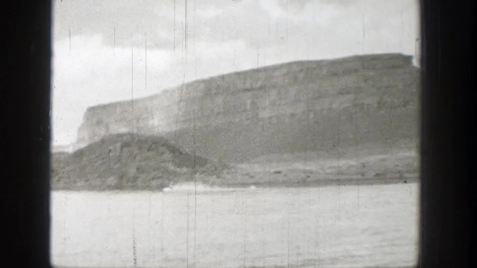 1938 Washington 8mm view of a mountain lake with a small pale object near the distant shoreline.