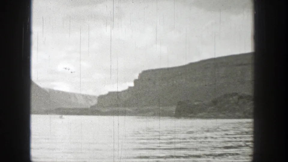 1938 Washington 8mm frame showing a wide lake, rugged cliff faces, cloudy sky, and visible film gate shadows.