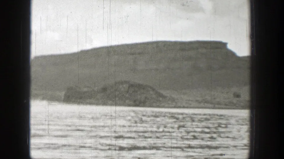 1938 Washington 8mm frame with a broad water surface, low shoreline, and distant bluff seen from a moving viewpoint.