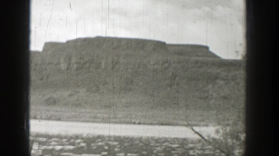 1938 Washington home-movie frame showing a rocky hill, shoreline, water, and dark window framing.
