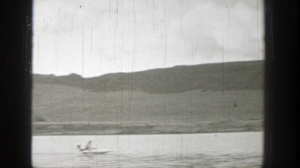 Washington 1938 8mm frame of open hills and water through dark window bars, with a small moving object near the shoreline.