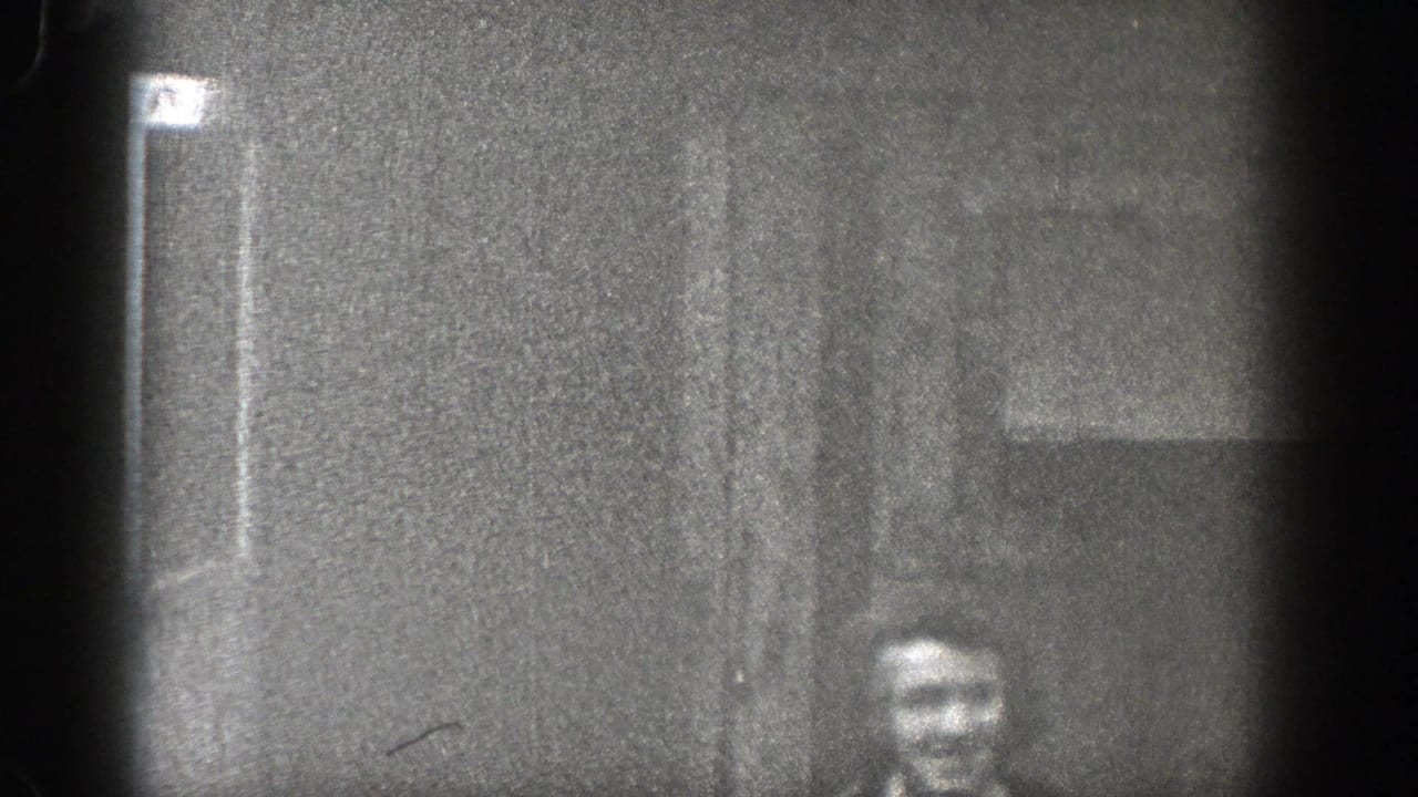 1938 Washington 8mm frame showing a woman partly visible near a dark wall or doorway, with heavy grain and vignetted film edges.