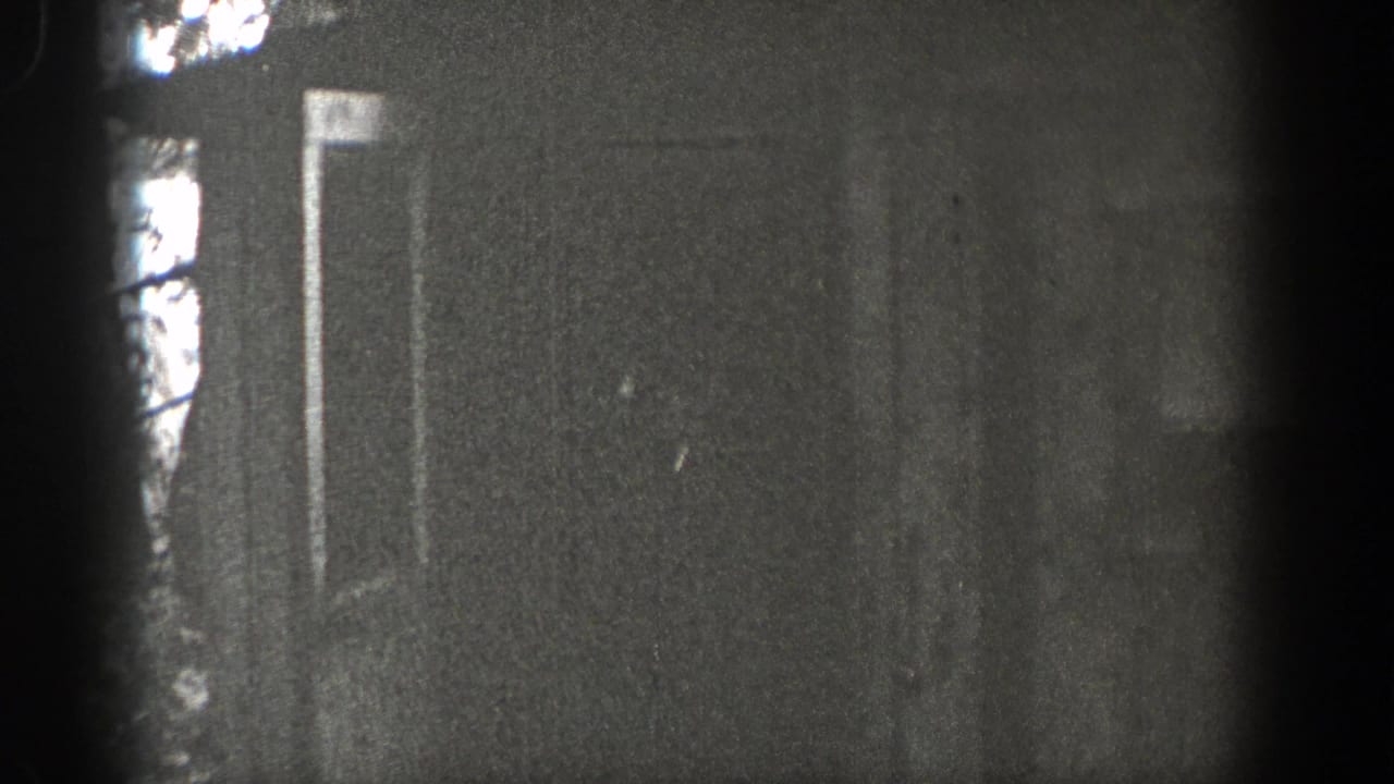 1938 Washington 8mm frame with a dim wall or doorway area, faint trees or exterior shapes, and strong dark film-edge vignetting.