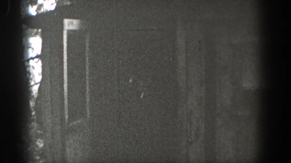 1938 Washington 8mm frame with a dim wall or doorway area, faint trees or exterior shapes, and strong dark film-edge vignetting.