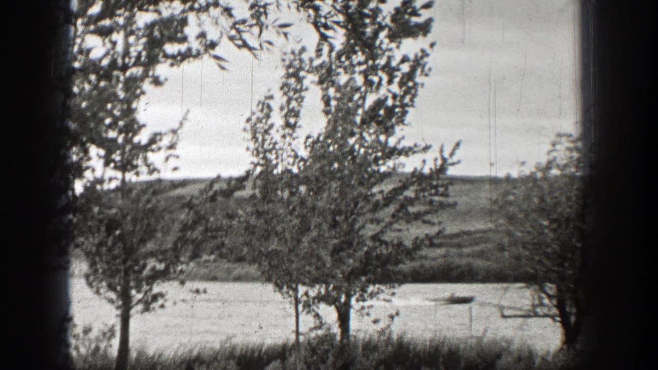 1938 home-movie frame of a breezy Washington waterfront, with trees, shoreline grass, and small boats on the water.