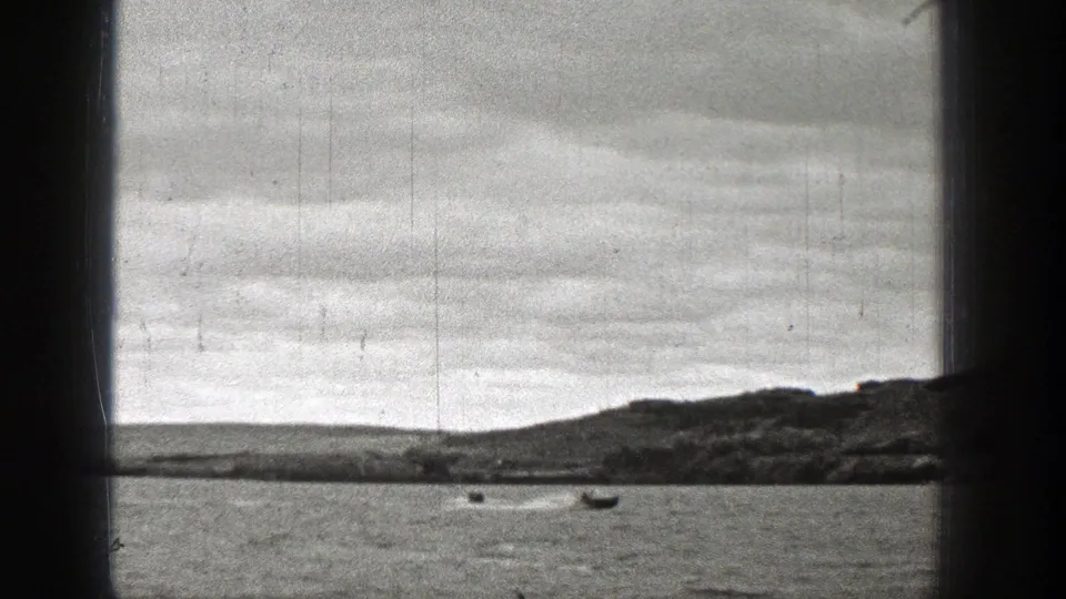 1938 Washington 8mm frame showing small boats on rippled water through a dark window frame, with low hills and cloudy sky beyond.