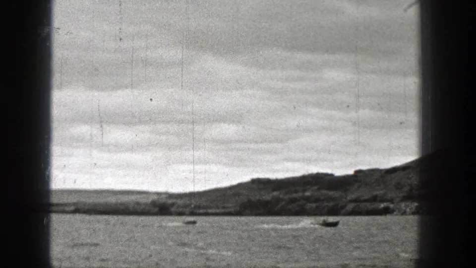 1938 Washington home-movie frame with a vertical window mullion, small boats on water, a low shoreline, and overcast sky.