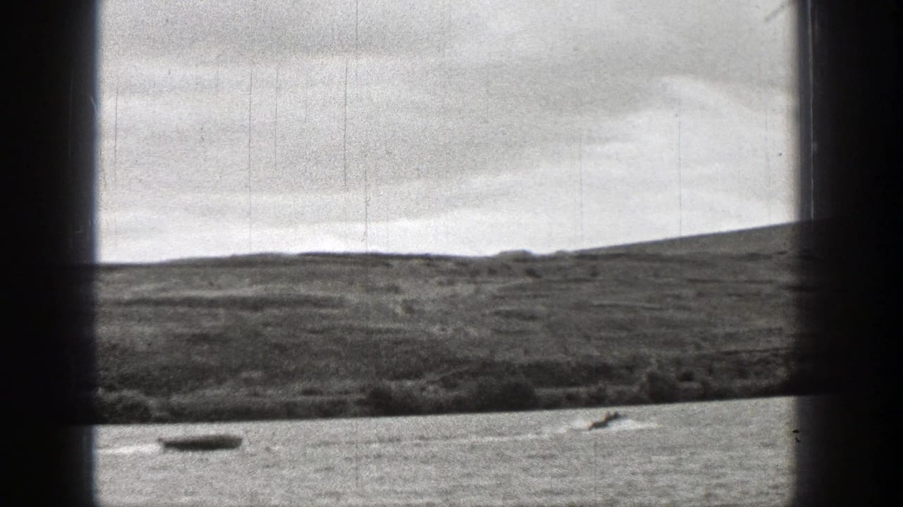 Small boat on a lake with a grassy shoreline and low hills beyond.