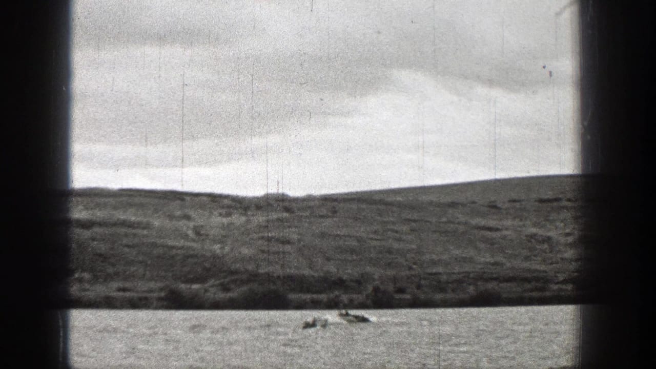 1938 Washington home-movie frame showing small distant boats on lake water below a grassy hillside.
