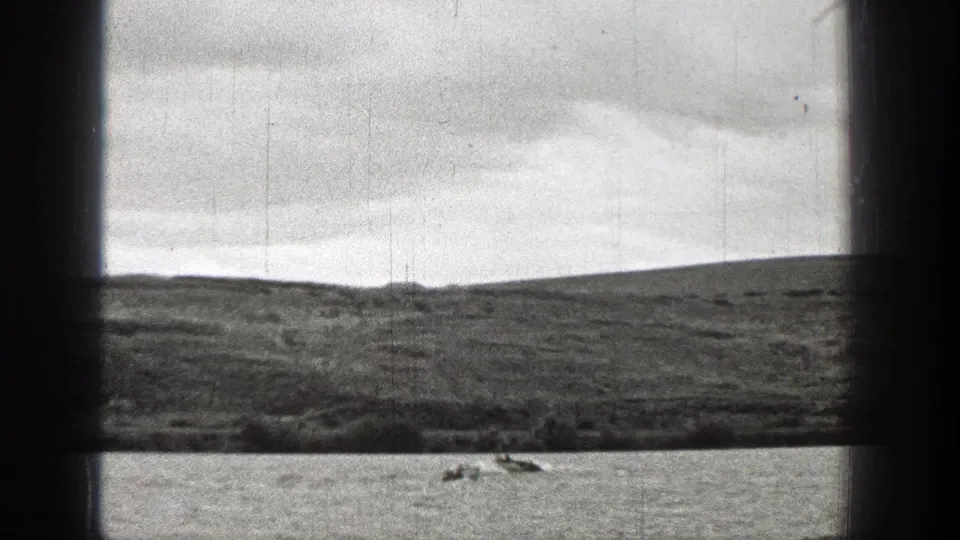 1938 Washington home-movie frame showing small distant boats on lake water below a grassy hillside.