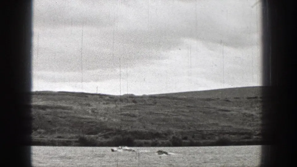 1938 Washington 8mm frame with small boats crossing lake water in front of open fields and low hills.