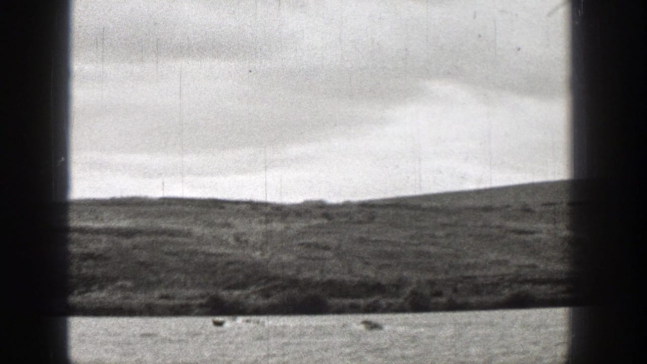 1938 Washington 8mm frame showing small boats moving across choppy water, viewed through dark vertical and horizontal bars with low hills beyond.
