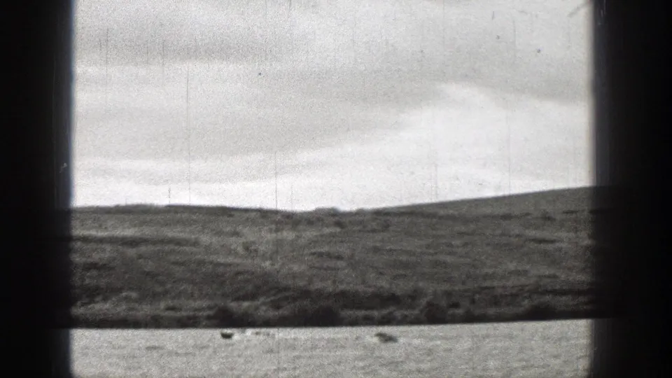 1938 Washington 8mm frame showing small boats moving across choppy water, viewed through dark vertical and horizontal bars with low hills beyond.