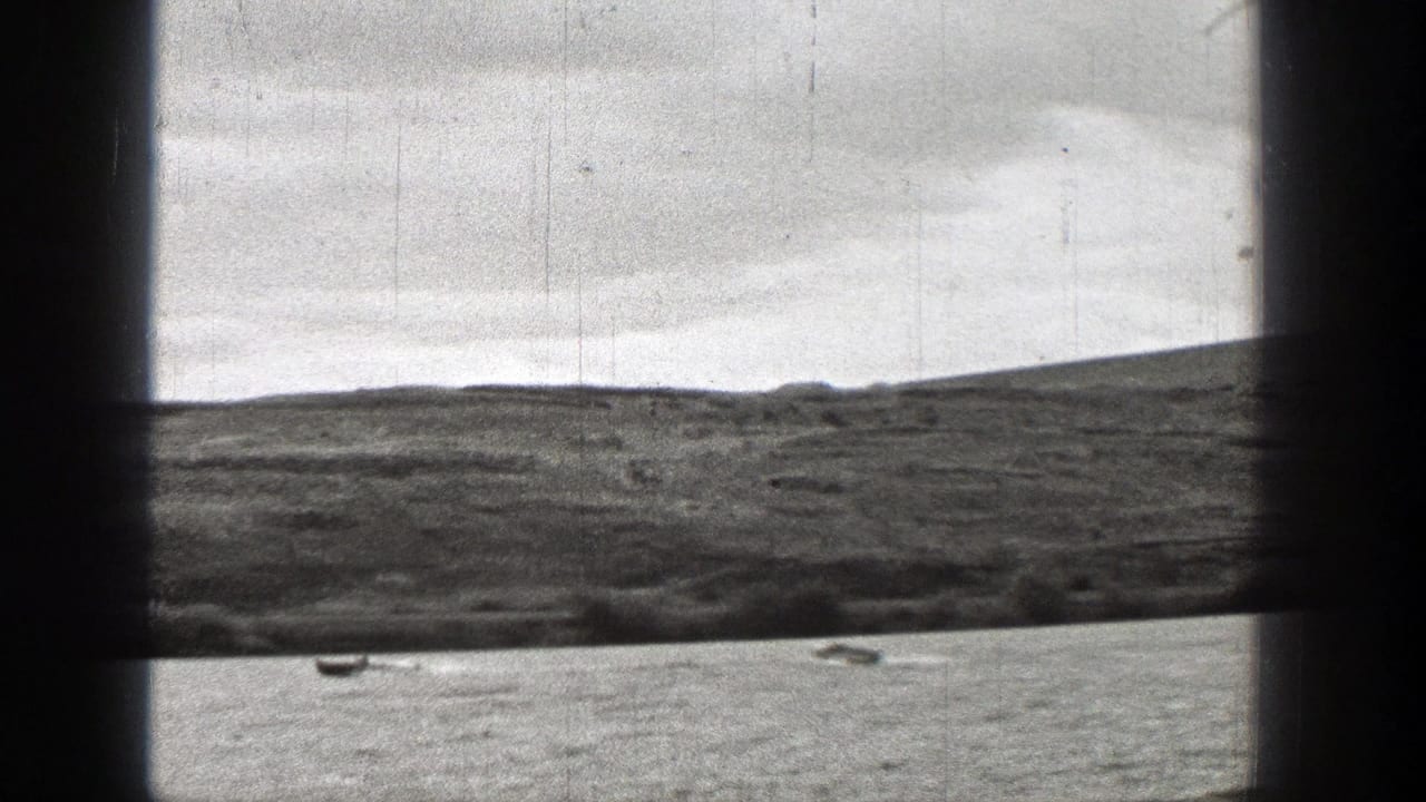 1938 Washington home-movie frame with distant small boats on open water, white wake marks, low hills, and dark foreground framing.