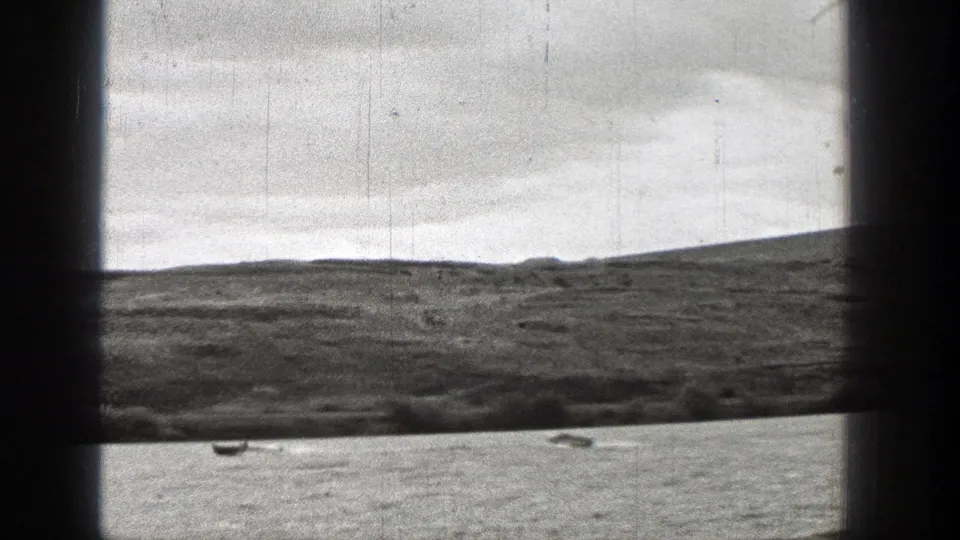 1938 Washington home-movie frame with distant small boats on open water, white wake marks, low hills, and dark foreground framing.