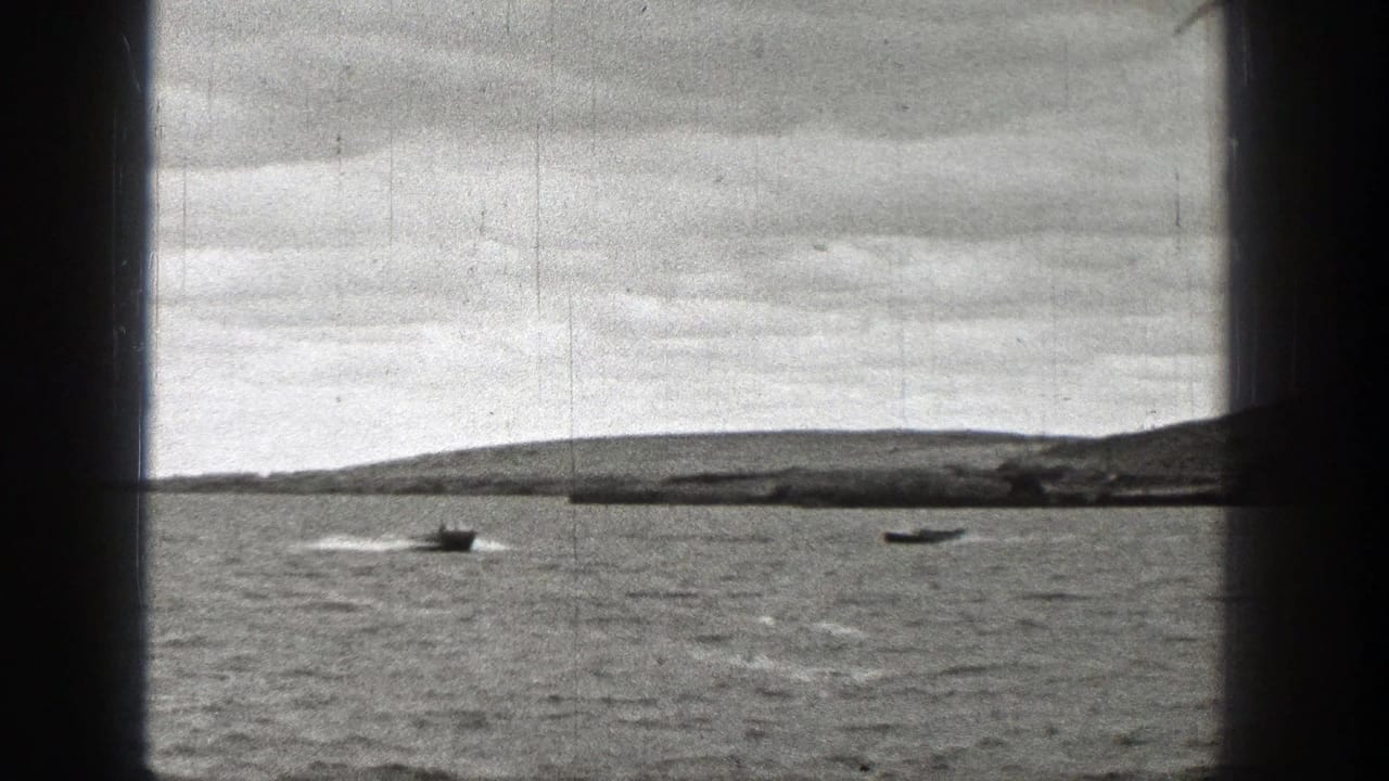 1938 Washington frame with two small boats moving across choppy water, their wakes visible below a low hilly shoreline and cloudy sky.