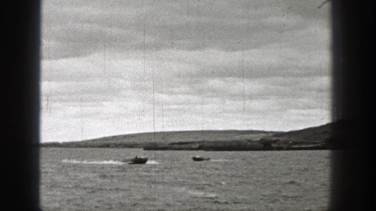 Two small boats move across a lake beneath a cloudy sky, seen through dark vertical frame borders.