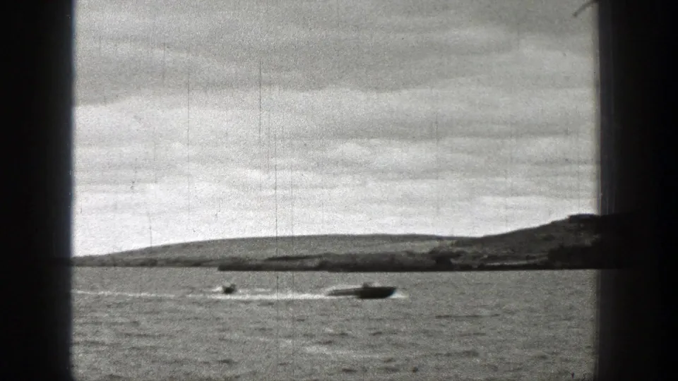1938 Washington 8mm frame with a speedboat cutting across lake water, another boat nearby, low hills, cloudy sky, and scratched film texture.