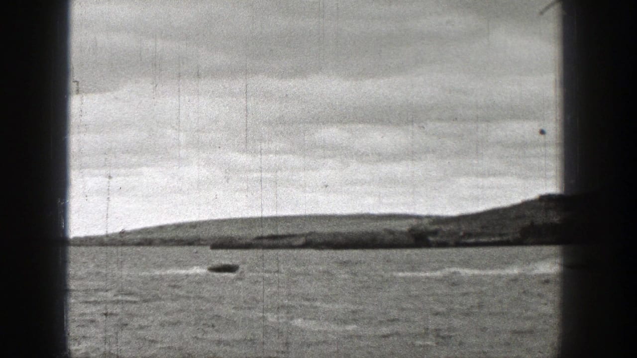1938 Washington home-movie frame showing one visible motorboat on open lake water, with a distant shoreline, cloudy sky, and dark frame edges.