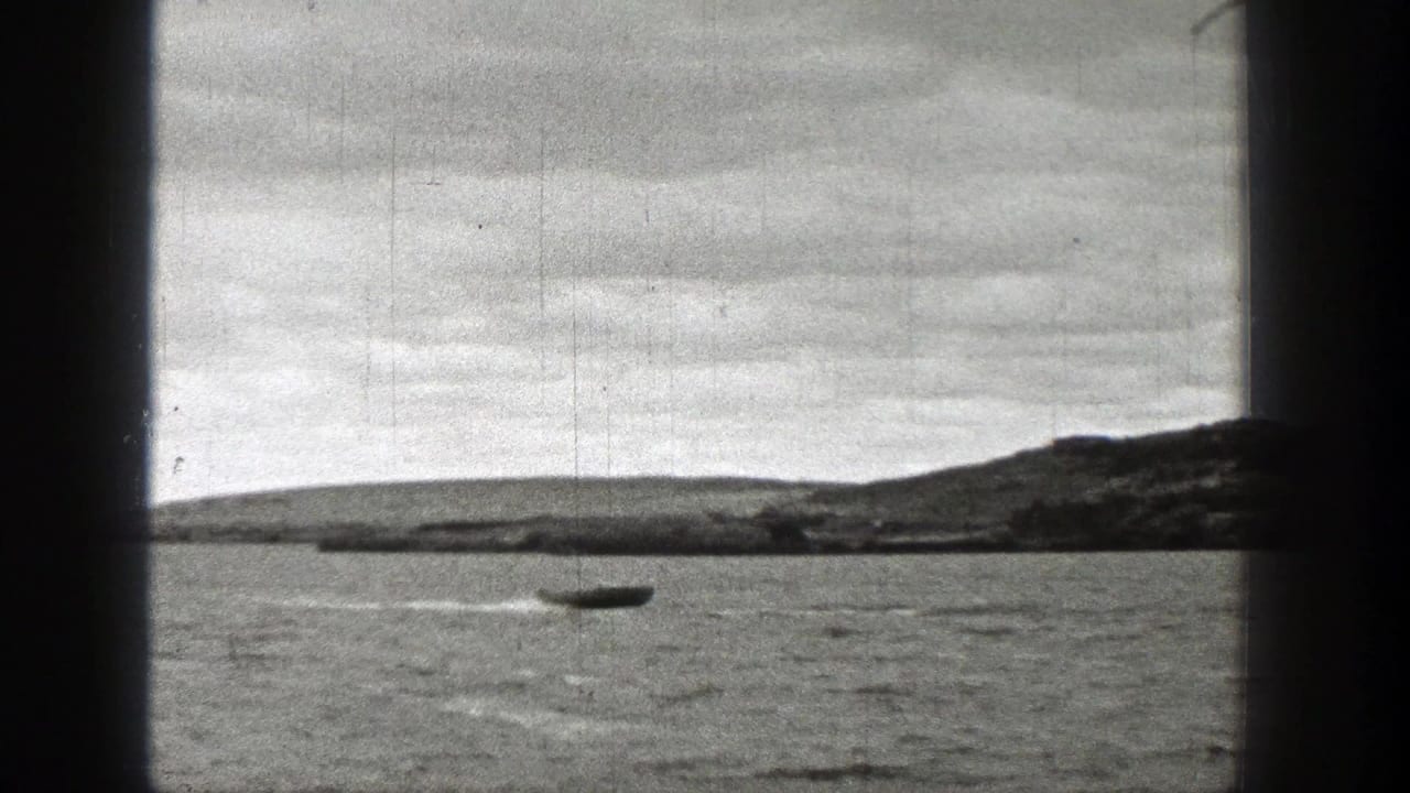1938 Washington 8mm frame of a small boat moving across a lake, framed by dark borders with visible grain, scratches, and overcast shoreline.