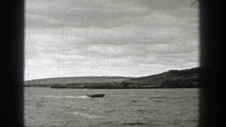 1938 Washington 8mm frame of a small boat moving across a lake, framed by dark borders with visible grain, scratches, and overcast shoreline.