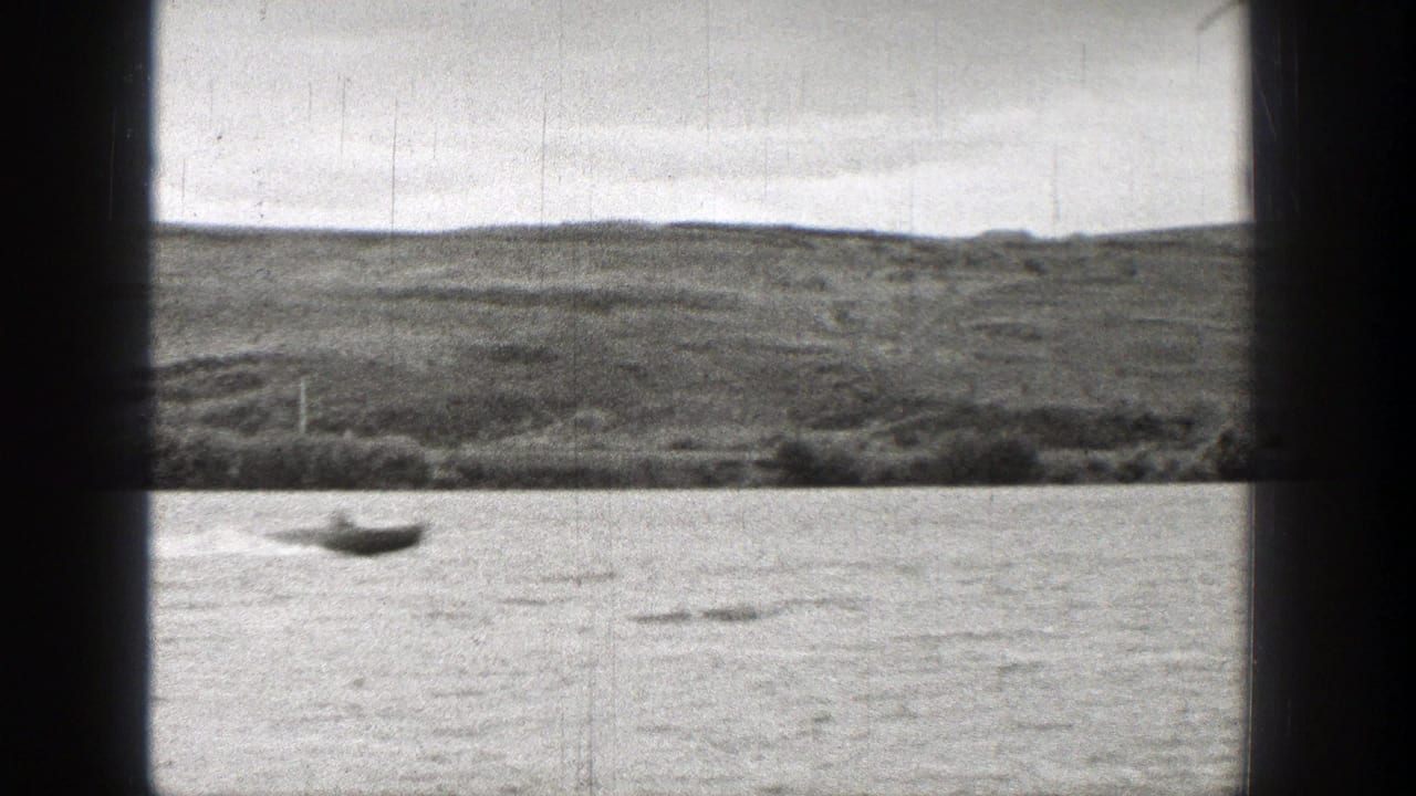 Small boat on open water with low shoreline behind it.