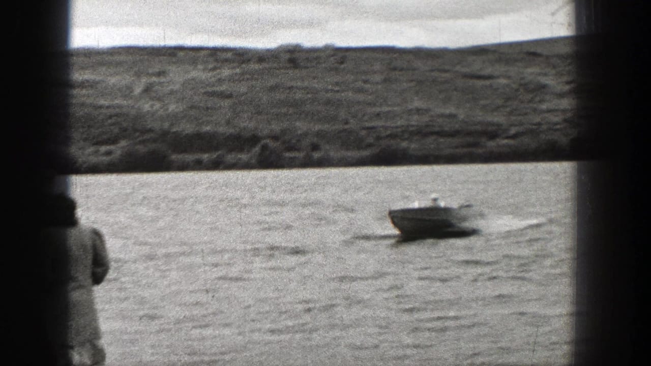 Small motorboat crossing Washington water in a 1938 home-movie view, with a partial spectator at the frame edge.