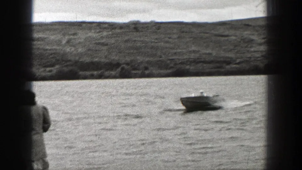 Small motorboat crossing Washington water in a 1938 home-movie view, with a partial spectator at the frame edge.