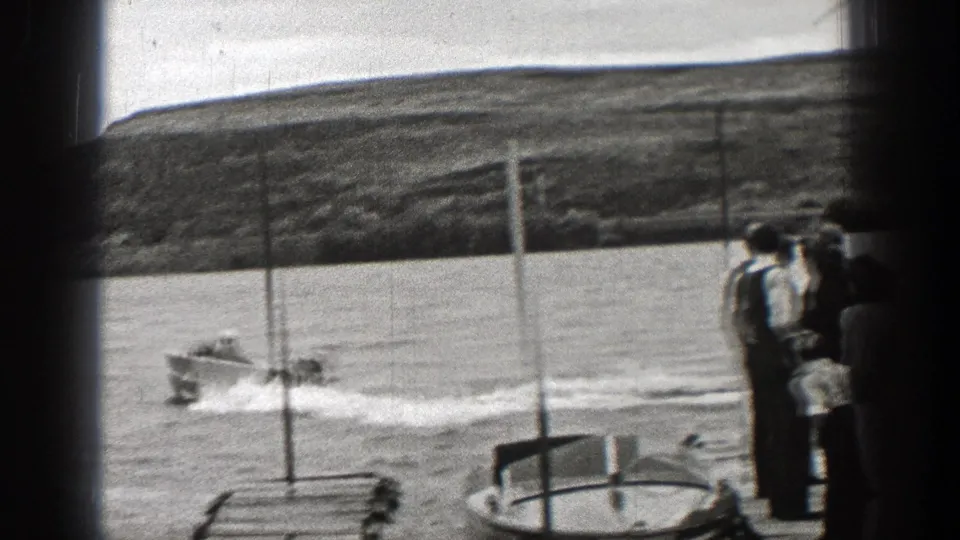 A small motorboat leaves a curved wake as Washington spectators watch from shore in 1938 home-movie footage.