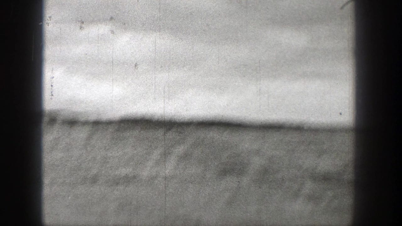 Overexposed Washington coastal view on 8mm film, with a faint shoreline and dark vertical frame shadows.